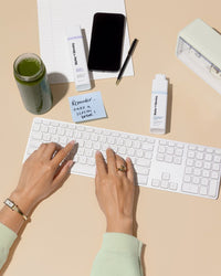 Person using a keyboard on a desk with a phone, Matter of Monday bottles, and other items.