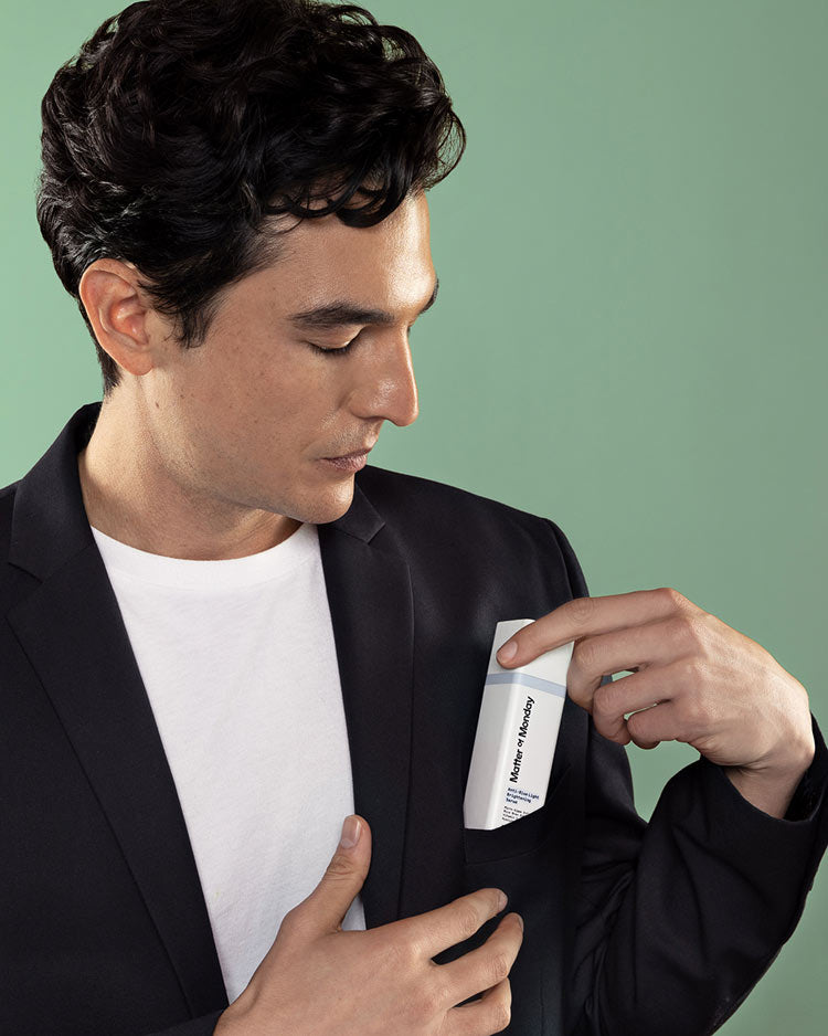 Man in a black suit with a white shirt holding a product packaging against a green background