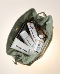 Green handbag with skincare products and glasses on a light background